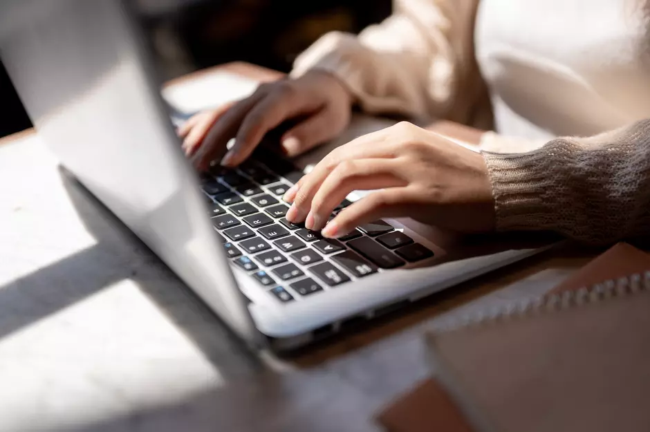 Dłoń piszącą na klawiaturze laptopa, ujęcie z boku z jasnym tłem, format banera