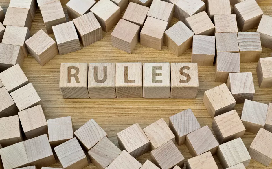 Napis "RULES" ustawiony z kostek, otoczony kostkami bez napisów, wszystko leżące na drewnianym blacie, 
